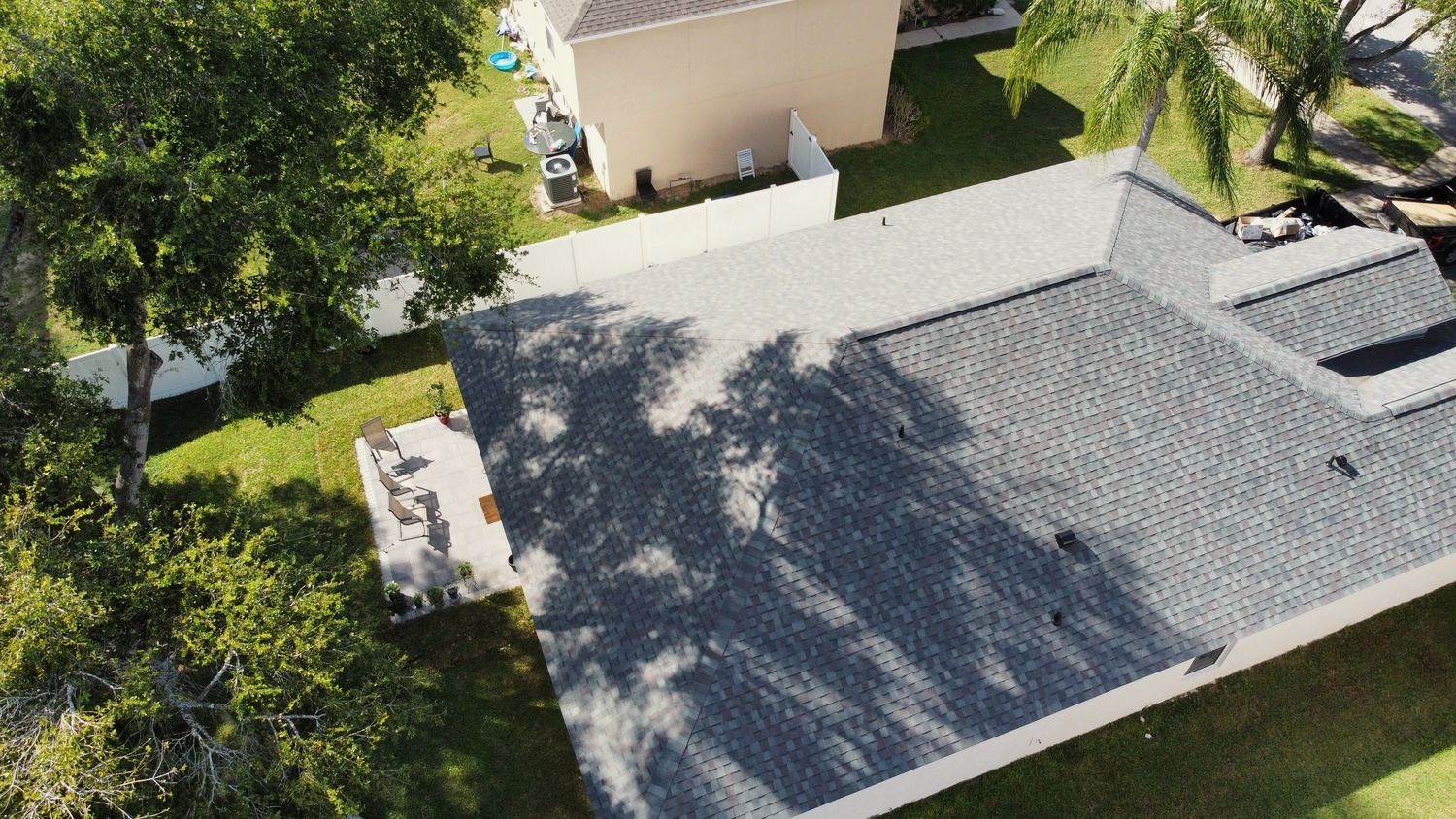 Drone view of a single-story home with a hip roof, a backyard patio and oak shade